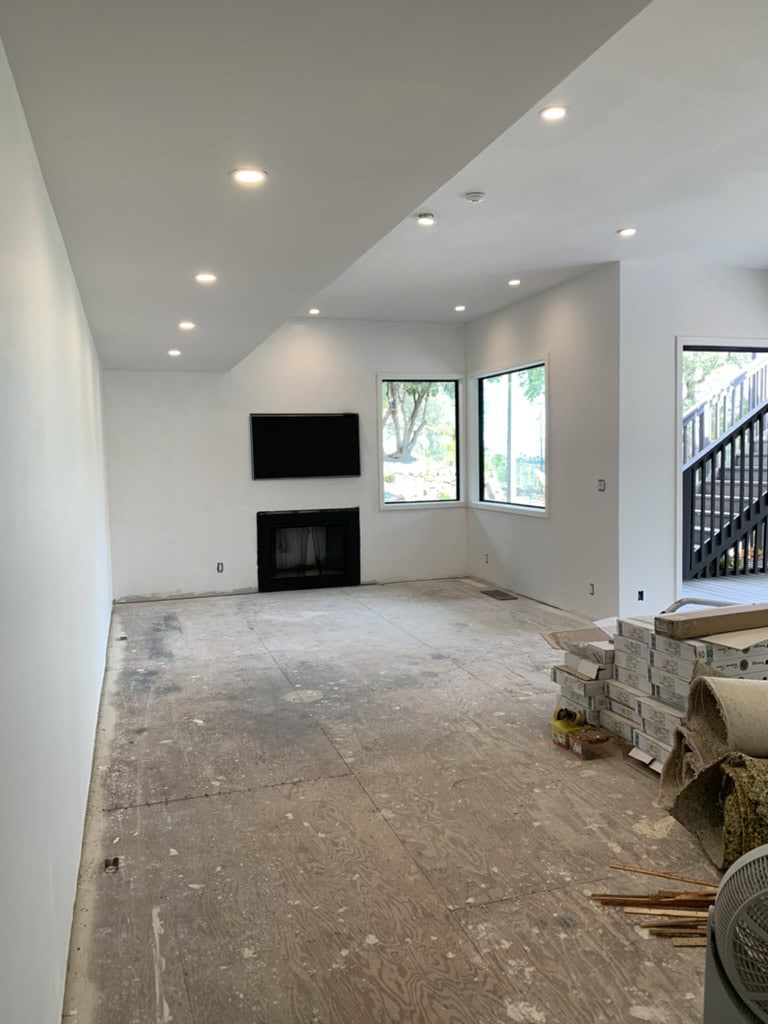 A spacious, unfurnished room with white walls, recessed lighting, a black television, and fireplace. Construction materials indicate ongoing renovation or decoration. This image was sent by a design-chat client for their problem solving package.