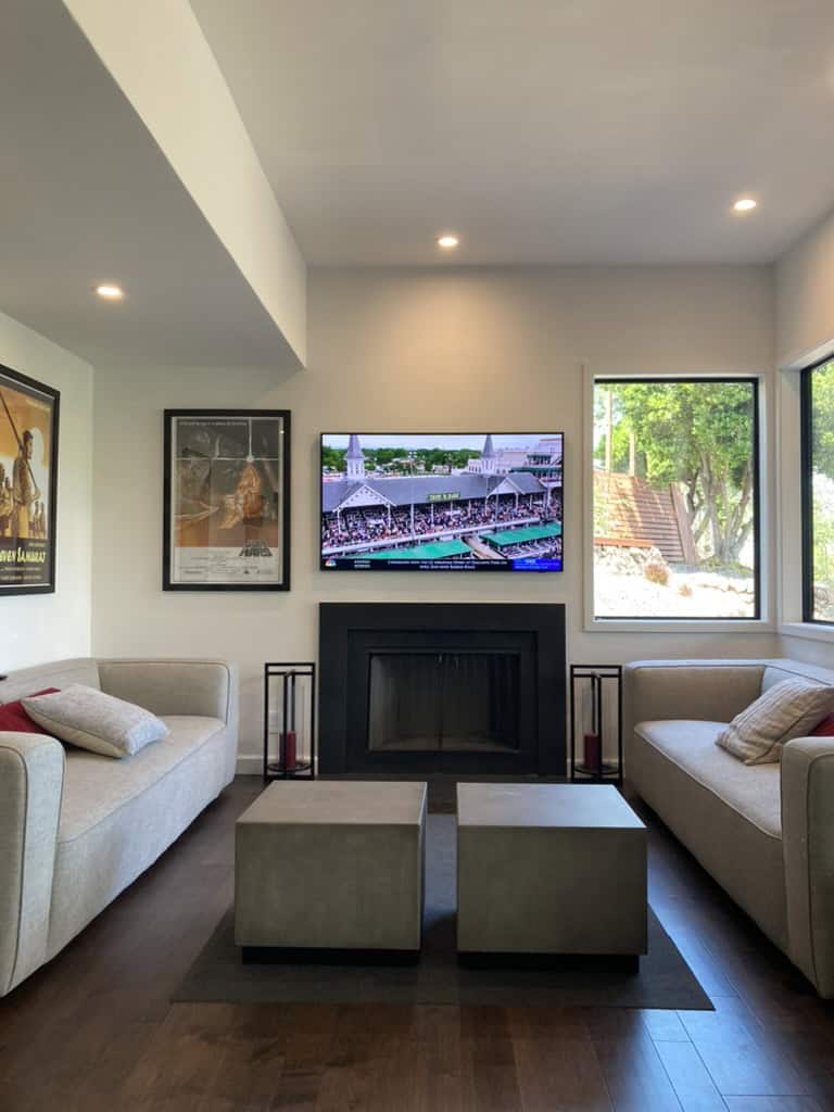 The image shows the final results of a problem solving project with design-chat. It features a modern living room with two sofas, a fireplace, a mounted television, two cube ottomans, and a framed poster on the wall.