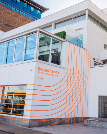 This image shows the former london design museum building's corner with orange lines creating a pattern stretching over a white background. A banner reads "Designed to Win." Part of a collection of inspirational images from Catherine Severson, the virtual interior designer who created design-chat.