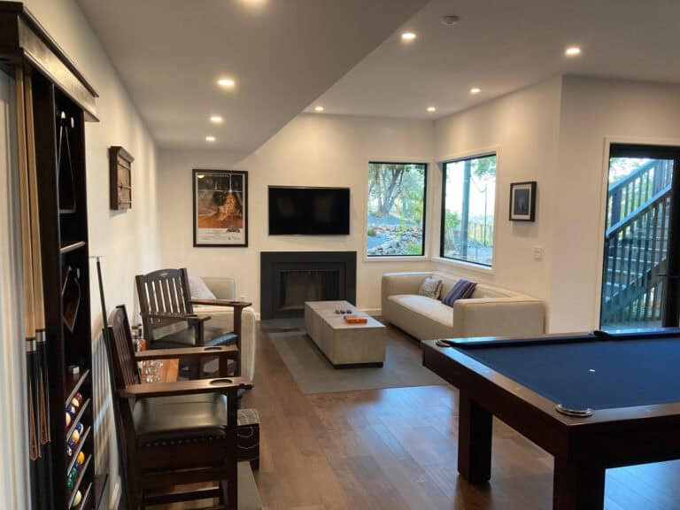 A modern living room featuring a billiards table, a cozy seating area with a sofa, a fireplace, mounted television, and framed wall art.