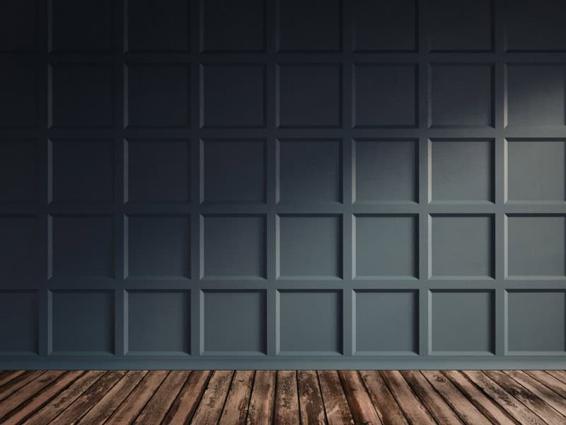 An empty room corner with a textured dark blue-gray square paneled wall and a brown wooden floor, implying a modern and sleek interior design.