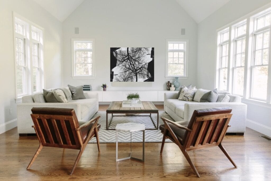 A spacious, bright living room with large windows, white sofas, wooden furniture, and a black and white tree artwork on the wall showcases a modern minimalist house interior design style.
