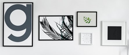 Five different framed artworks are displayed on a white wall, featuring abstract designs, botanical prints, and a numeral in a minimalist arrangement. Demonstrating stylish home decor on a budget.