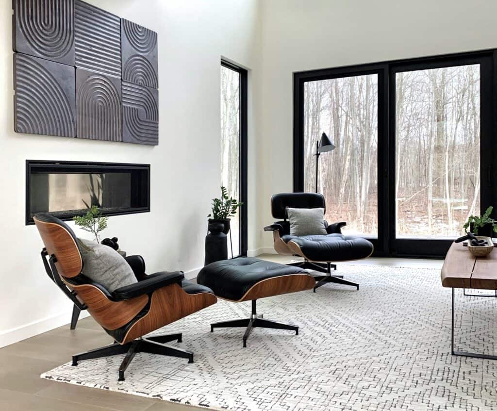 Modern minimalist house design living room with two elegant black chairs, geometric wall art, minimalist fireplace, large windows, wooden table, and decorative plants.